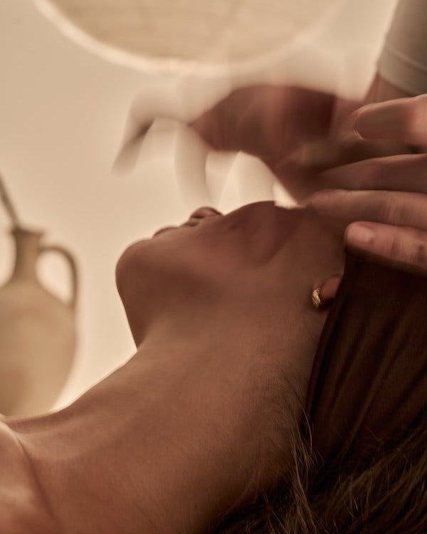 Close-up of a person's face with hands gently holding it, in a warm-toned setting.