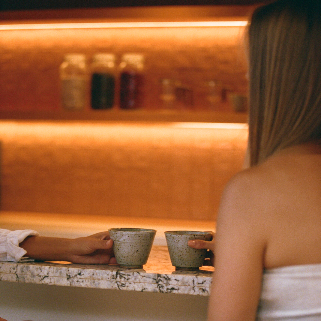 Two people sitting at a bar, each holding a cup, with a warm, inviting ambiance.